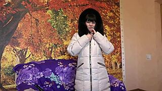 A mature woman in a fur-trimmed hood sucks a large dildo passionately.