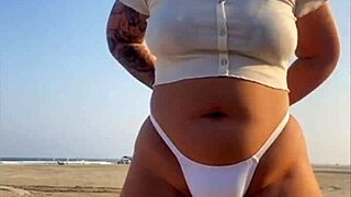 Redhead exhibitionist flashes swollen pussy lips on beach, muscular guy watches intently