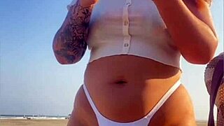 Redhead exhibitionist flashes swollen pussy lips on beach, muscular guy watches intently