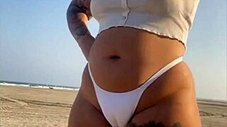 Redhead exhibitionist flashes swollen pussy lips on beach, muscular guy watches intently