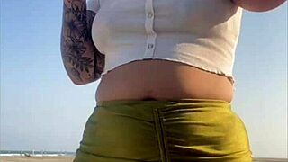 Redhead exhibitionist flashes swollen pussy lips on beach, muscular guy watches intently